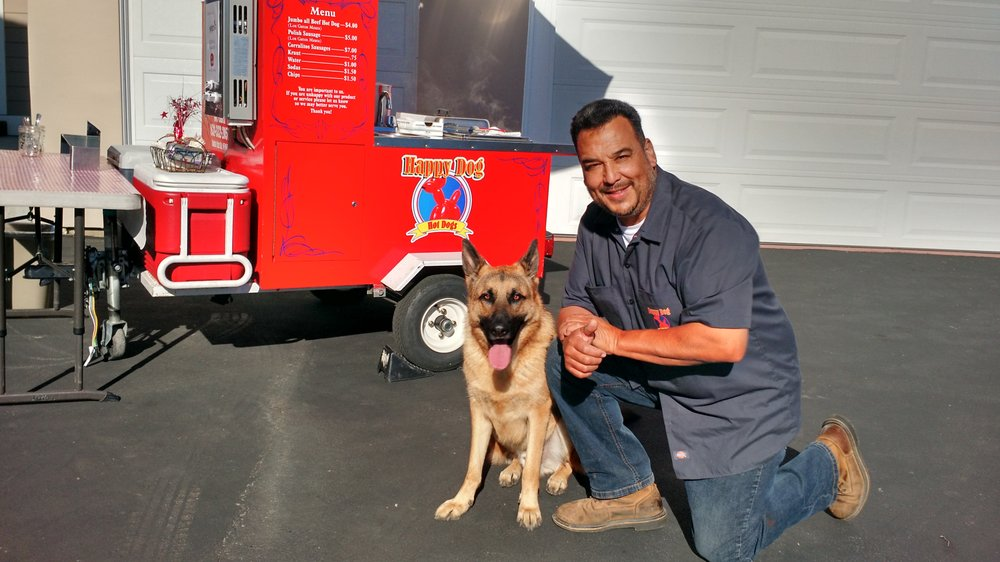 Happy Dog Hotdogs owner with his German Shepherd dog in front of the red food cart